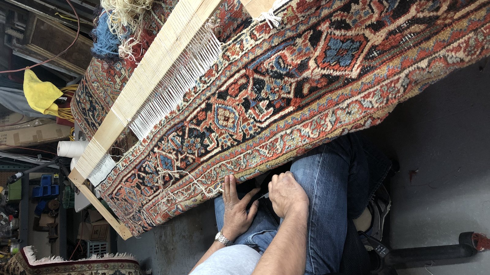 Hands reweaving wool back into a rug foundation at the workshop bench